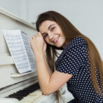 portrait-smiling-young-woman-leaning-piano-looking-camera